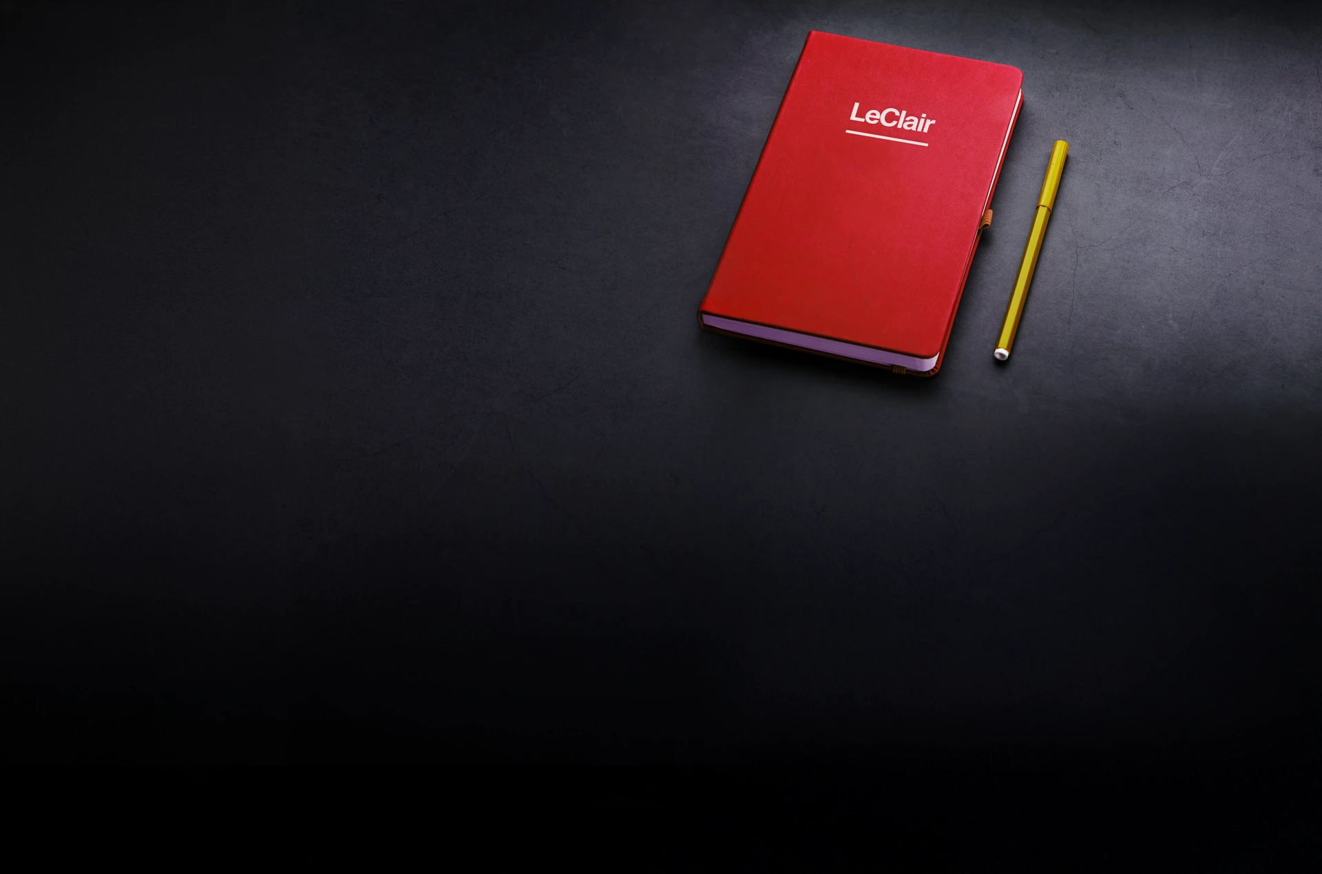 LeClair branded red notebook with pen on dark table